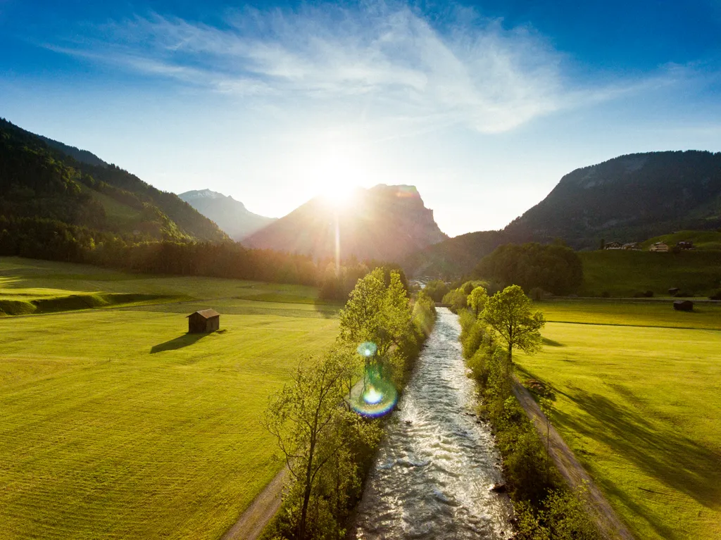 Sonnenaufgang über dem Tal von Schoppernau mit Bergbach und Wiesen